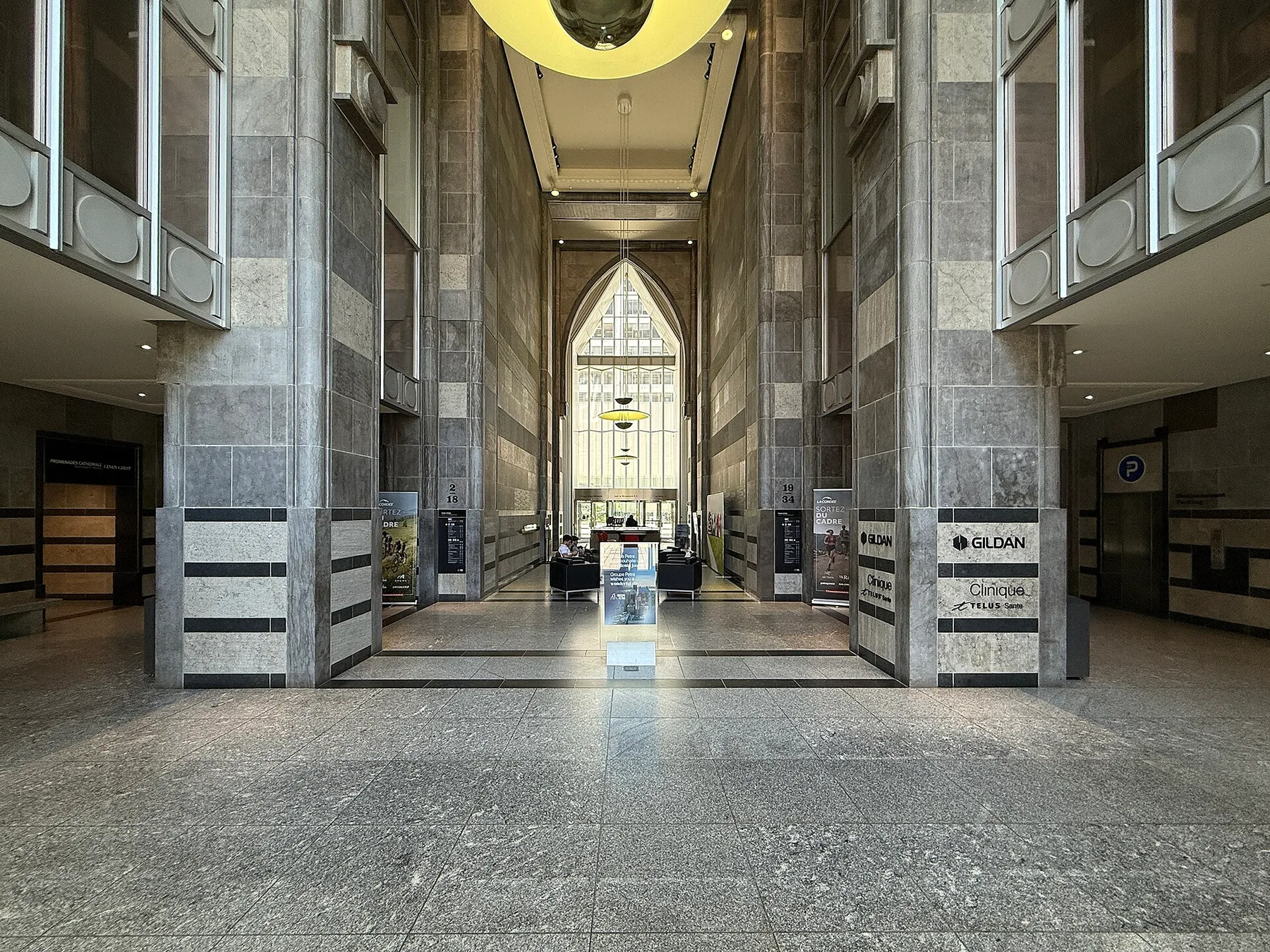 A tall stone-clad commercial lobby with glazed walls and geometric detailing