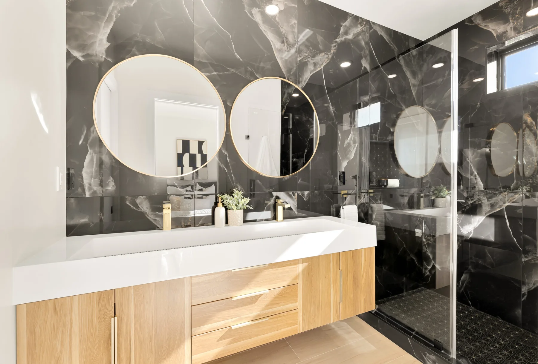 A double vanity with circular mirrors and a dark tile feature wall